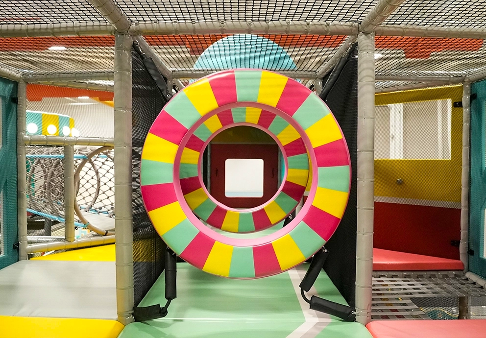 A view looking through colorful striped ring obstacles inside the multi-level indoor playground climbing structure at playtropolis