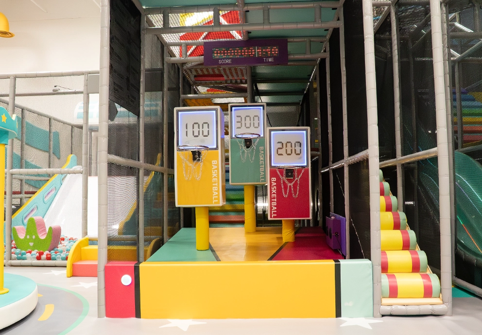 Three electronic arcade-style basketball hoops with digital score displays inside the indoor playground sports zone at playtropolis