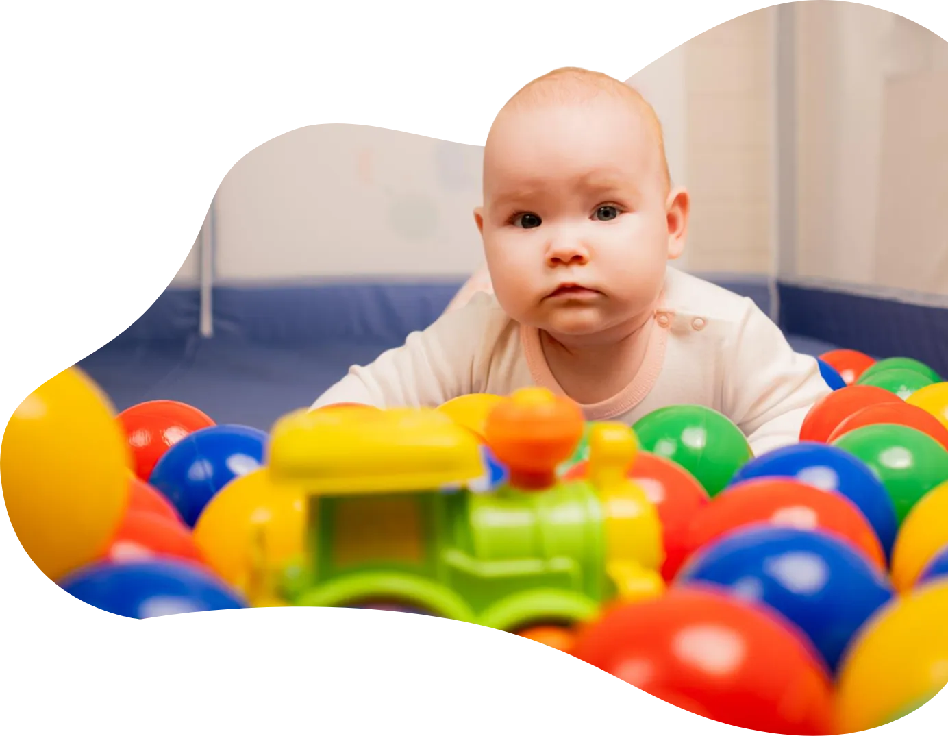 Playtropolis-baby-soft-play-woodbridgewebp - playtropolis Baby in a white onesie sits among colorful plastic balls in a ball pit, looking at the camera.