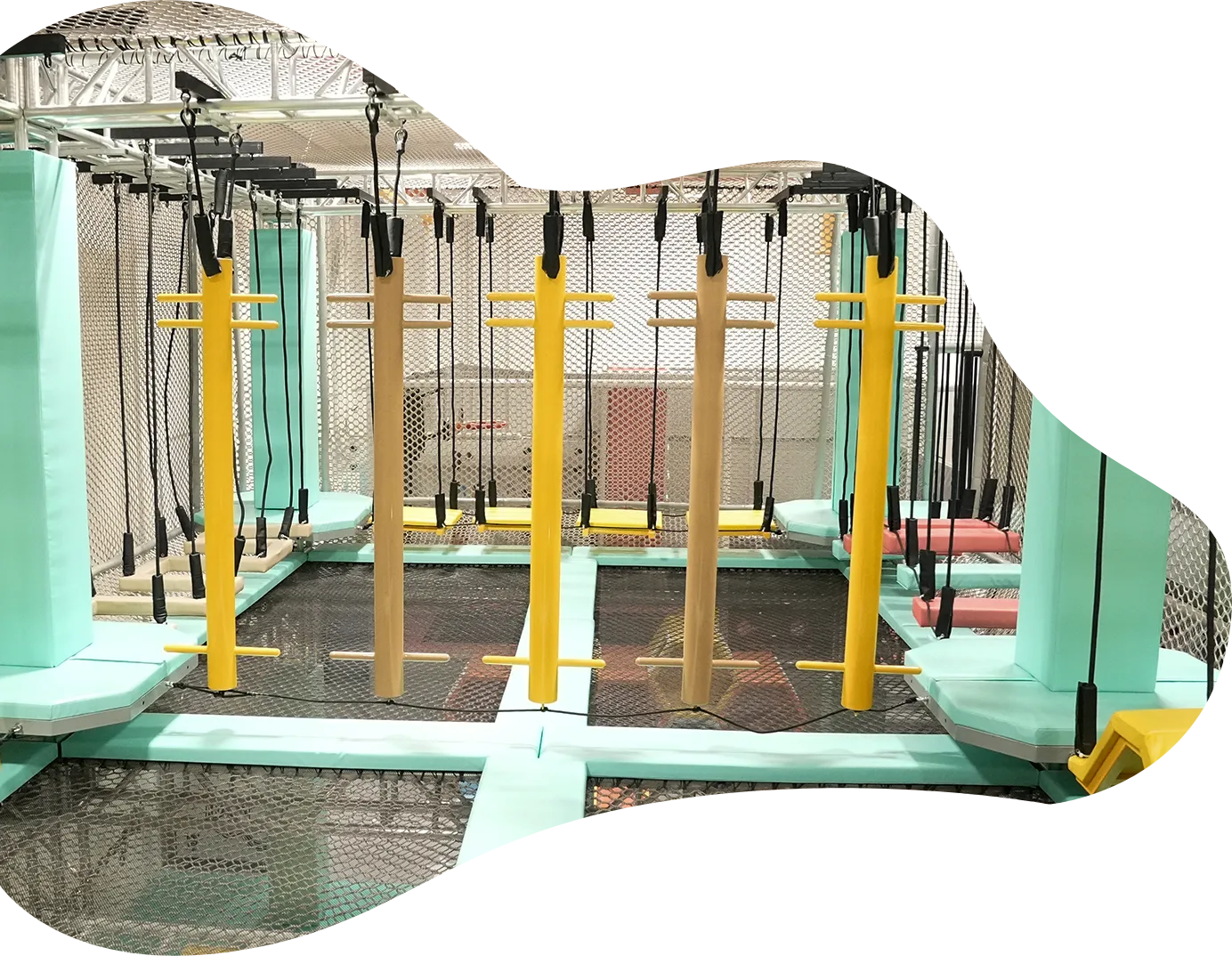 Playtropolis-ninja-warrior-hanging-steps-woodbridgewebp - playtropolis Indoor trampoline park obstacle course with hanging handles and yellow vertical posts between mint-green padded rails.